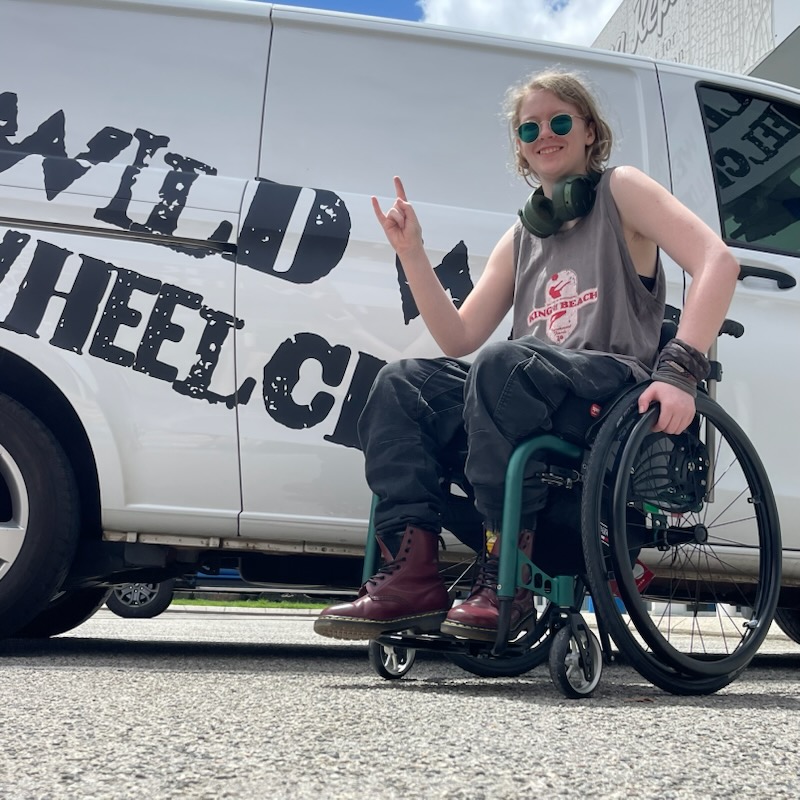 Acacia, a member of Team Artistic Disorder, in her wheelchair in front of a Wild West Wheelchairs van