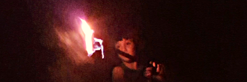 A young fire twirler holding a flame in the dark
