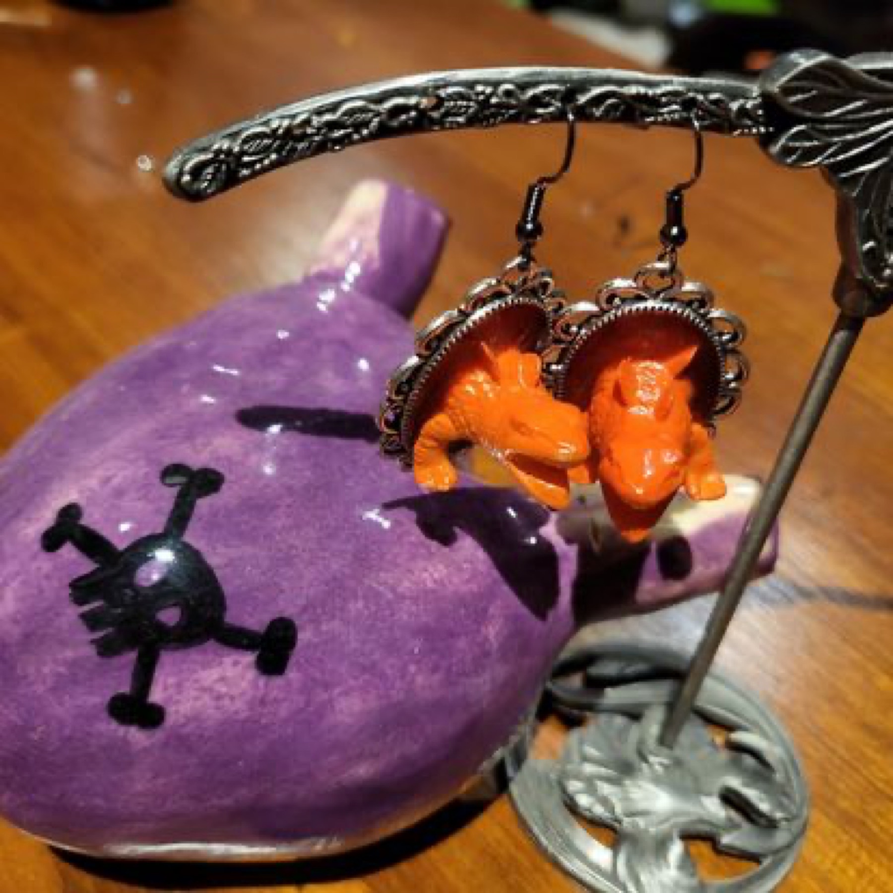 Orange dinosaur toy earrings beside a purple ceramic heart